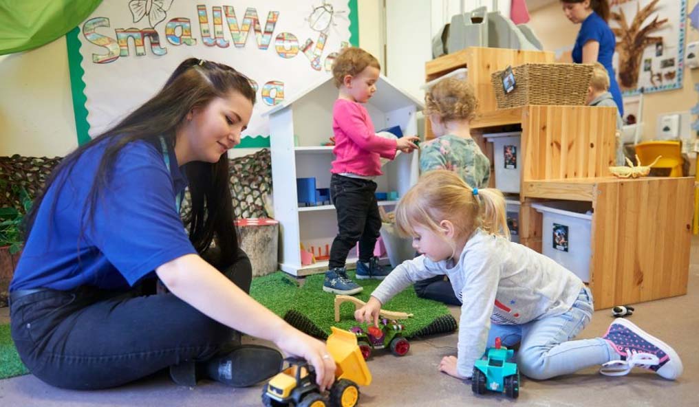 A yound student playing with toddler and toy digger