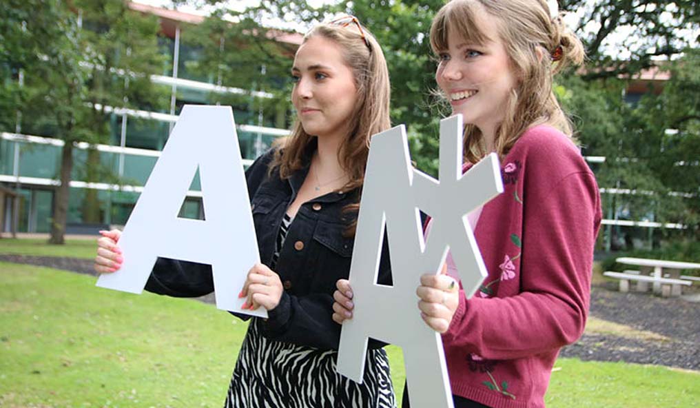 Two female students holding cutouts of their grades A and A*